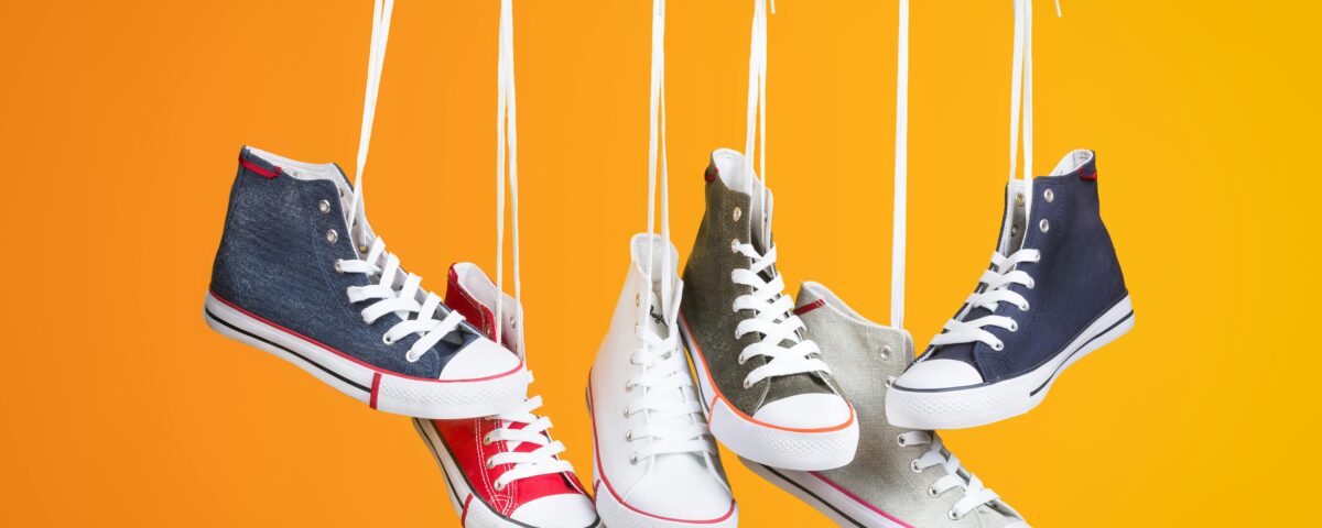 Stylish sneakers in various colors hanging with laces on a vivid orange backdrop. Ideal for fashion themes.